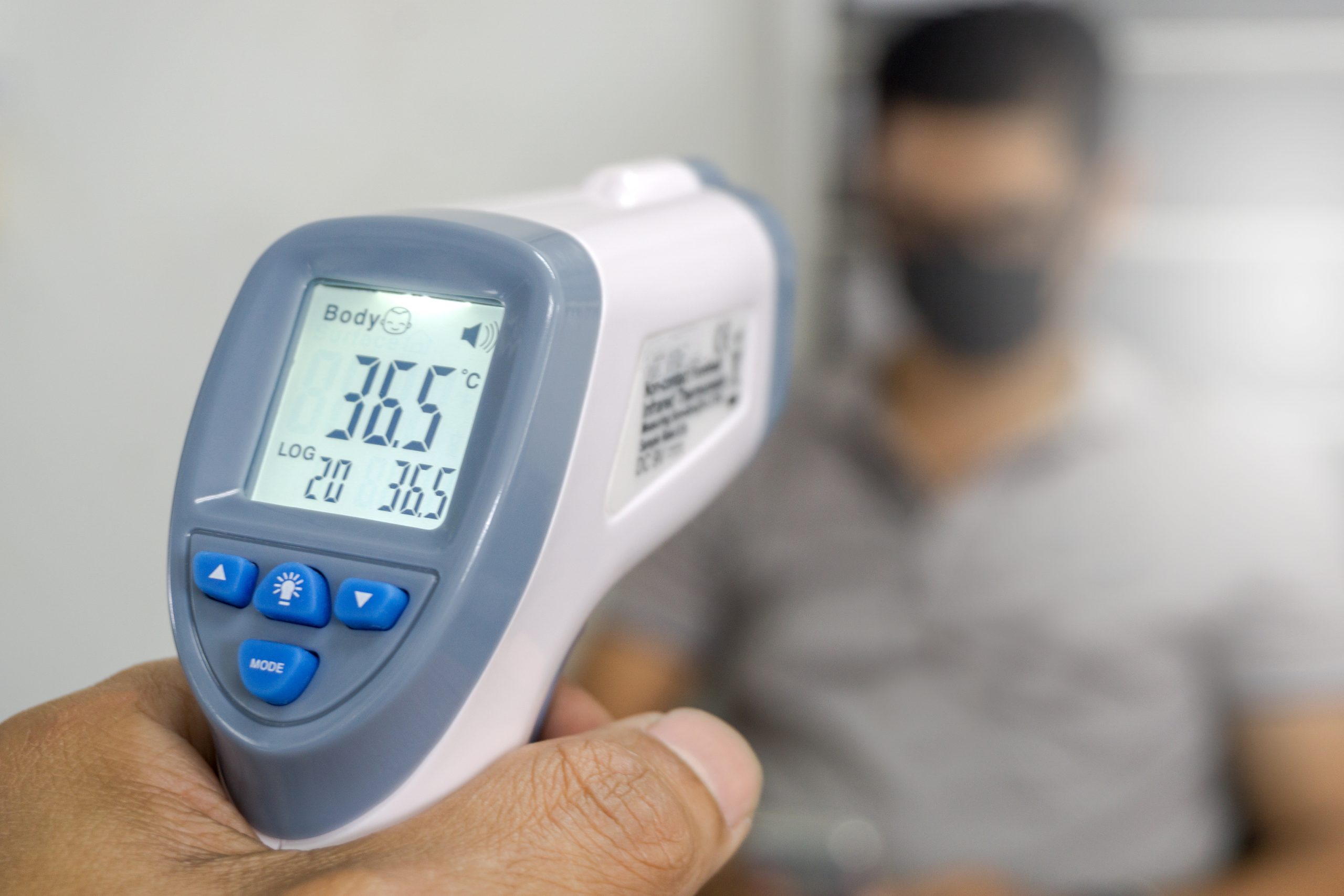 Hand holding infrared thermometer to measuring temperature on blurred asia people with face mask on background. Covid flu screening 19 concept.