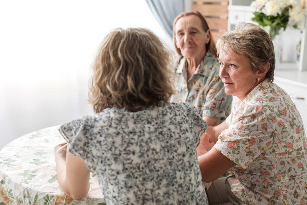 Three women engaged in conversation at a table, to encourage independence and collaboration among themselves
