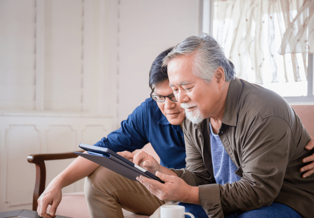 An Asian man and his father engaged in using a tablet computer together, sharing a moment of technology and connection.