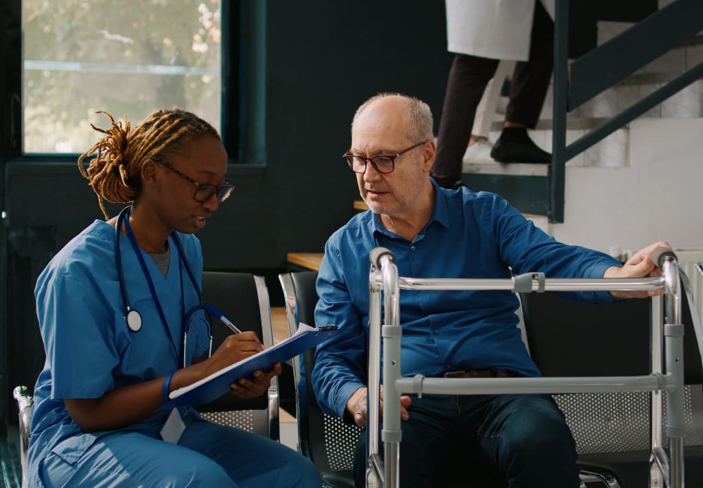 A nurse and an elderly resident are seated together in a chair, engaged in a conversation in a care home setting.