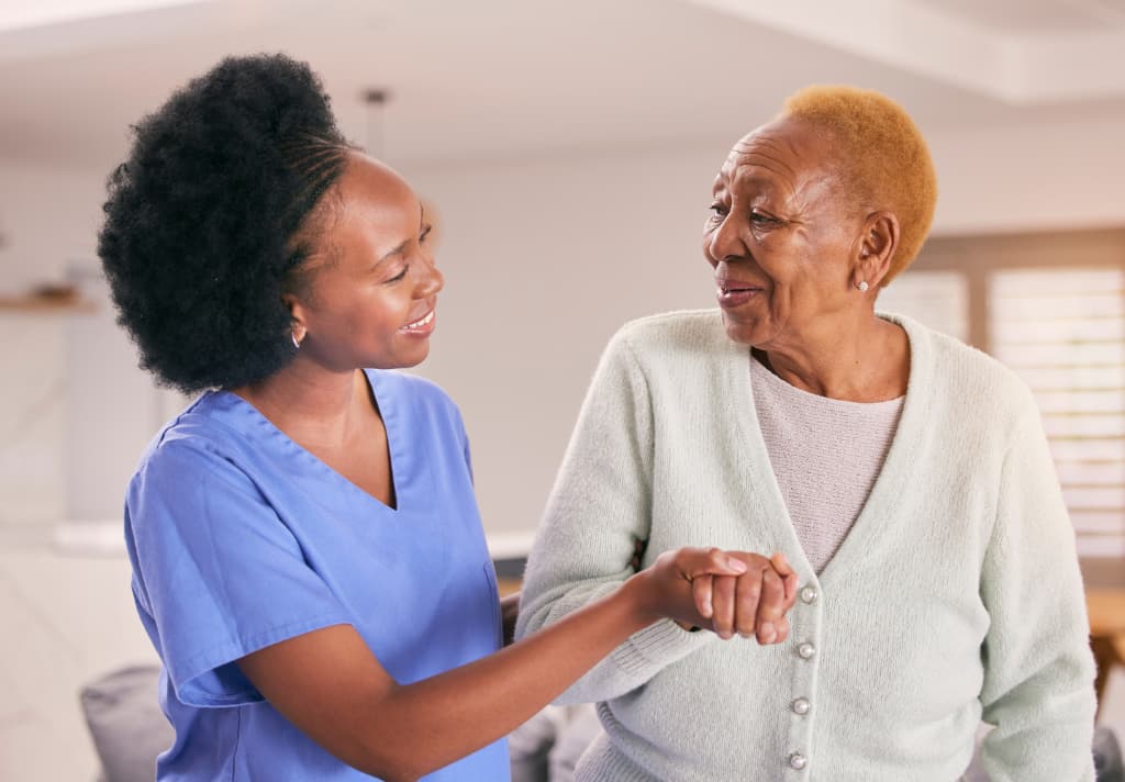 A nurse gently holds hands with an elderly woman, conveying care and compassion in a care home setting