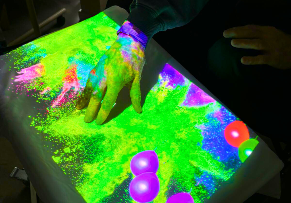 A person interacts with a glowing table, creating colourful light patterns in a dimly lit room.